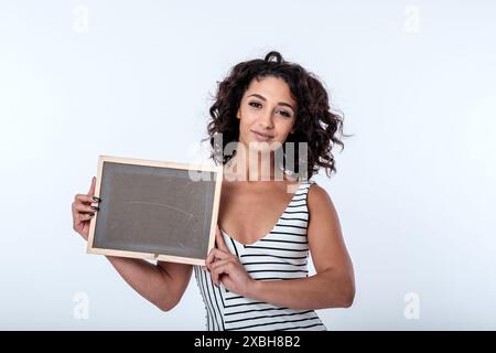 Una giovane donna d'affari, fiduciosa e accogliente, sorridente, ha un cartello con la lavagna con spazio per lo slogan pubblicitario o la messaggistica di concetto chiave. Copia spazio Foto Stock