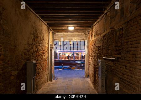 Città di Venezia, Italia, antico passaggio con pareti in mattoni invecchiati e soffitto a travi in legno, illuminato da una singola lampada nel quartiere di Cannaregio di notte Foto Stock