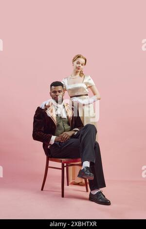 Classico ritratto nobile di gentiluomo regale con un ricco cappotto di velluto, con la signora in piedi con fiducia dietro di lui su sfondo rosa studio Foto Stock