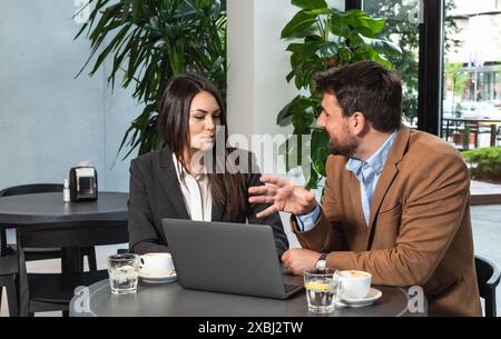 Due giovani colleghi, uomo d'affari e donna d'affari seduti in una caffetteria che lavorano insieme su un computer portatile. Lavoro di squadra di uomini d'affari in caffetteria, cervelli Foto Stock