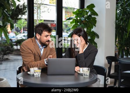 Due giovani colleghi, uomo d'affari e donna d'affari seduti in una caffetteria che lavorano insieme su un computer portatile. Lavoro di squadra di uomini d'affari in caffetteria, cervelli Foto Stock