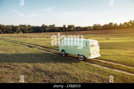 Volkswagen Transporter classico verde su strada in auto - vista aerea. Pulmino su strada sterrata dritta tra fienili. Foto Stock