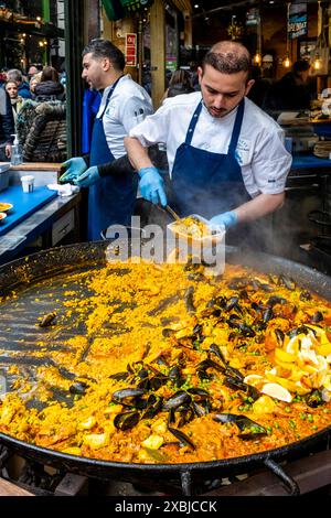 Un giovane che serve Paella da Un piatto grande al Borough Market, Londra, Regno Unito. Foto Stock