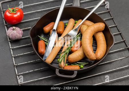 Salsicce e ciuffi di rosmarino con coltello e forchetta in padella su griglia metallica. Pasta di pomodoro, pomodoro e garlik in tavola. Sfondo nero. Vista dall'alto Foto Stock