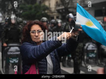 Buenos Aires, Argentina. 12 giugno 2024. Una donna con una bandiera argentina sbatte su una pentola di fronte a una fila di poliziotti durante una dimostrazione contro un progetto di riforma del governo ultraliberale. Credito: Fernando Gens/dpa/Alamy Live News Foto Stock