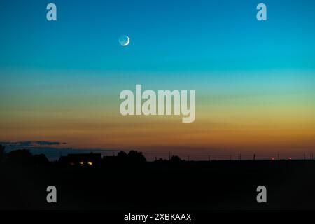 Una falce luna è visibile in un cielo serale splendidamente colorato. Foto Stock