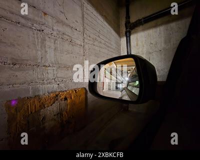 Specchio laterale di un'auto che riflette un parcheggio inferiore in un grande edificio. Foto Stock