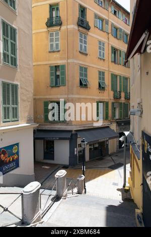 Nizza, Francia - 12 giugno 2024: Un'affascinante scena di strada nella città vecchia di Nizza, con edifici color pastello con persiane verdi e un piccolo negozio Foto Stock