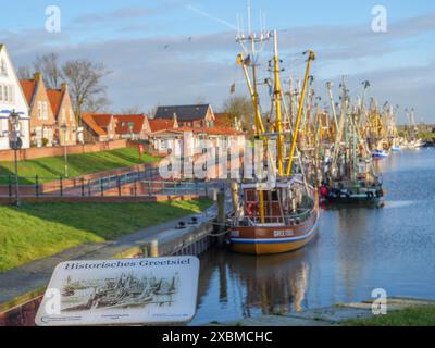 Un porto con diverse barche da pesca, case sullo sfondo e un cielo azzurro limpido, greetsiel, frisia orientale, germania Foto Stock