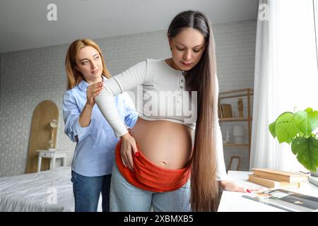 Doula matura massaggia una donna incinta con sciarpa in camera da letto Foto Stock