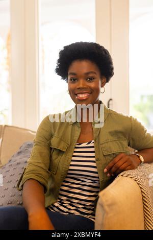 Donna afroamericana seduta sul divano, sorridente calorosamente, a casa Foto Stock