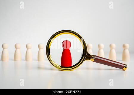 Una lente d'ingrandimento che guarda alle persone in legno rosso, seleziona una persona nella squadra. Risorse umane. Ricerca di un nuovo membro del team. Opportunità di lavoro assunta co Foto Stock