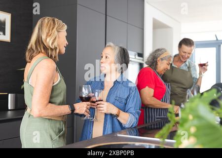 Gruppo di donne mature che amano il vino e chiacchierano in cucina moderna Foto Stock