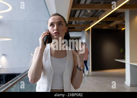 Donna caucasica che parla sullo smartphone, sembra preoccupata nel moderno corridoio dell'ufficio, copia spazio Foto Stock