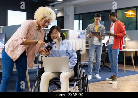 Colleghi di diverse origini collaborano utilizzando la tecnologia in un ambiente moderno di startup Foto Stock