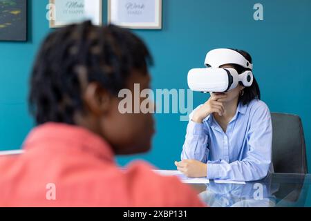 La donna asiatica usa il visore VR mentre l'uomo afroamericano osserva il lavoro di squadra di startup Foto Stock