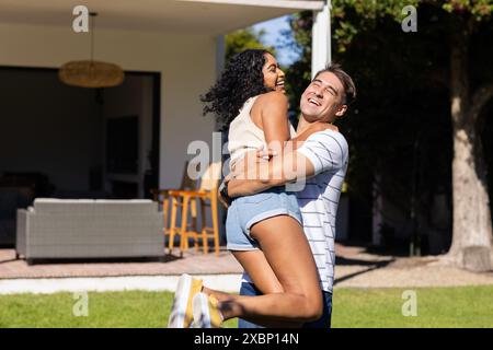 Giovane uomo caucasico che solleva e sorride al suo partner asiatico in un abbraccio giocoso, copia spazio Foto Stock