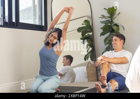 Giovani coppie diverse che praticano yoga insieme a casa in una stanza luminosa Foto Stock