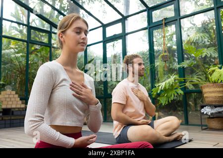 Uomo e donna caucasici che praticano yoga insieme nella casa di vetro Foto Stock