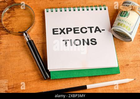 Iscrizione aspettative parola in un taccuino in una composizione con una lente d'ingrandimento, dollari e una matita Foto Stock