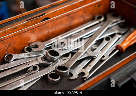 Angolo elevato di utensili e strumenti meccanici assortiti insieme a un cacciavite posizionato in una scatola sporca di olio in officina su sfondo sfocato Foto Stock