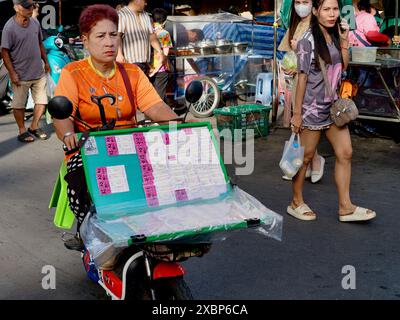 Una venditrice di biglietti della lotteria mobile, che vende i biglietti della lotteria nazionale, cavalca sullo scooter attraverso un mercato di Bangkok, Thailandia Foto Stock