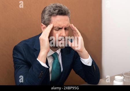 Uomo stressato con mal di testa. Un uomo d'affari stanco lavora straordinari e ha mal di testa. Uomo con notebook sul posto di lavoro, soffre di mal di testa. Emicrania da Foto Stock