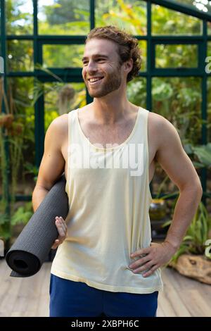 Praticante di yoga maschile caucasico con tappetino da yoga e sorridente Foto Stock