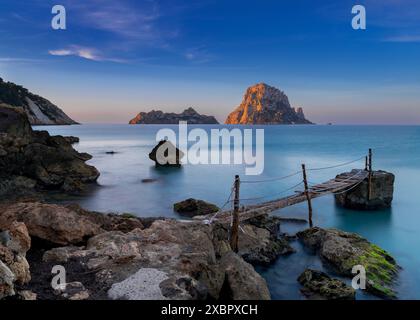 Un piccolo molo in legno a Cala d'Hort con vista sulle rocce di es Vedra sullo sfondo all'alba Foto Stock