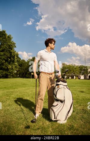 Un uomo si erge su un campo erboso con una borsa da golf, incarnando uno stile di vita di classe superiore in un elegante golf club. Foto Stock