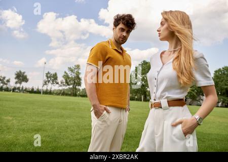 Un uomo e una donna eleganti vestiti con abiti eleganti si uniscono in un campo verde lussureggiante, che incarnano uno stile di vita lussuoso. Foto Stock