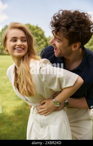 Una bella giovane coppia in abiti eleganti si posa graziosamente in un lussureggiante parco verde, trasudando un senso di stile vecchio denaro e stile di vita ricco di persone. Foto Stock