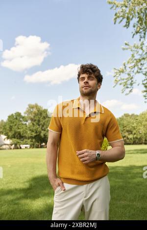 Un uomo con una vivace polo gialla si erge elegantemente in un campo verde lussureggiante sotto il caldo sole del mattino. Foto Stock