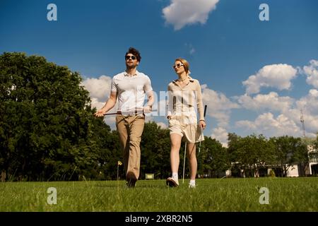 Una giovane coppia elegante in un elegante abbigliamento passeggia attraverso un lussureggiante campo erboso in un ambiente da golf club. Foto Stock