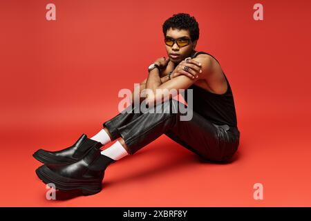 Uomo afroamericano in occhiali da sole seduto su sfondo rosso. Foto Stock