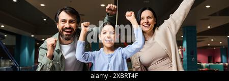 Una famiglia felice alza le braccia in una zona di gioco dei centri commerciali, celebrando l'unità e la felicità durante un weekend. Foto Stock