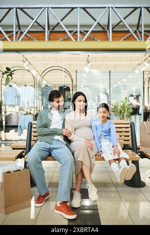 Una famiglia felice, vestita in modo informale, si siede insieme su una panchina in un vivace centro commerciale, prendendosi una pausa dallo shopping. Foto Stock