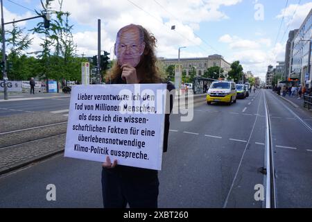 Berlino, Germania. 13 giugno 2024. Gli attivisti di Berlino hanno concluso uno sciopero della fame di 99 giorni il 13 giugno 2024 per costringere il governo federale del Cancelliere Olaf Scholz a riconoscere l'esistenza di una catastrofe climatica e poi bloccato il traffico su una strada principale, Berlino, Germania. Nella foto è raffigurato un attivista che indossa una maschera del Cancelliere Olaf Scholz e che tiene uno striscione in cui si dice che Scholz preferirebbe che milioni di persone morissero piuttosto che dichiarare i fatti scientifici sulla necessaria politica di protezione del clima. Crediti: Ales Zapotocky/CTK Photo/Alamy Live News Foto Stock