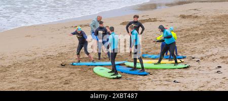Gli istruttori di surf guidano gli insegnanti del Surf Sanctuary insegnando a un gruppo di principianti di surf a Fistral Beach a Newquay in Cornovaglia nel Regno Unito Foto Stock