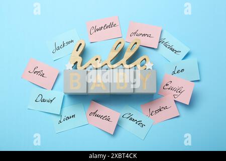 Cubi con la frase Hello Baby e adesivi di carta con nomi diversi su sfondo azzurro, piatto. Scegliere il nome del bambino Foto Stock