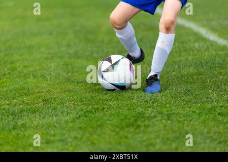 Pallone da calcio di un giovane giocatore di calcio. Palla e gambe in primo piano su un campo verde lussureggiante Foto Stock