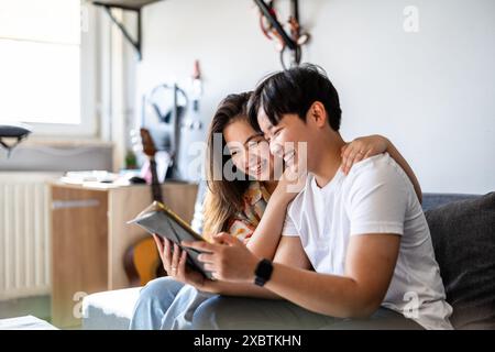 Felice giovane coppia che utilizza un tablet digitale insieme sul divano di casa Foto Stock