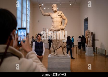 Un turista asiatico scatta una foto con uno smartphone accanto a una statua in marmo bianco di Poseidone di Milos, il dio greco del mare, presso l'Archaeo Nazionale Foto Stock