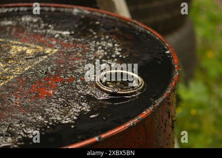 un barile rosso metallico si trova sulla strada cosparso di liquido nero, l'olio scuro scorre lungo il barile Foto Stock