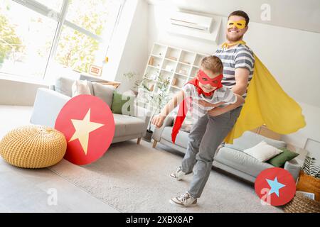 Bambino con suo padre in costumi da supereroe che si diverte a casa Foto Stock