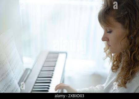 Giovane donna in abiti bianchi seduta e che suona un pianoforte elettronico Foto Stock