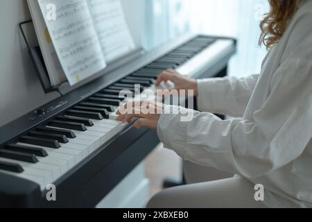 Giovane donna in abiti bianchi seduta e che suona un pianoforte elettronico Foto Stock