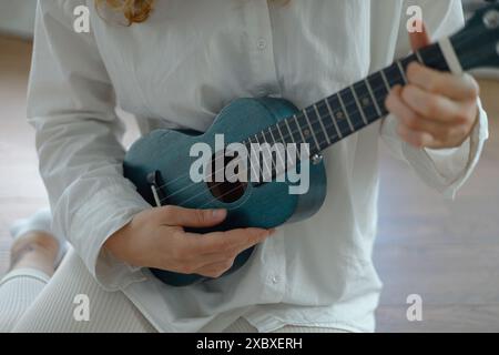 primo piano di un ukulele nelle mani di una ragazza con una camicia bianca Foto Stock