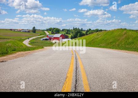 Fattoria con un fienile rosso su una strada curvilinea nella campagna dell'Iowa in una brillante giornata primaverile Foto Stock