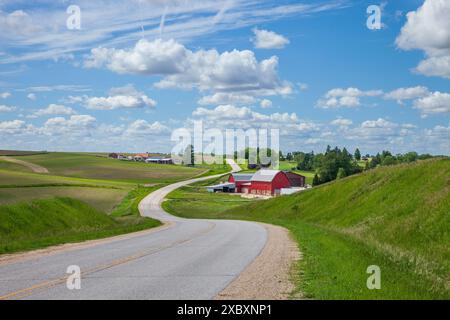 Fattoria con un fienile rosso su una strada curvilinea nella campagna dell'Iowa in una splendida giornata primaverile Foto Stock